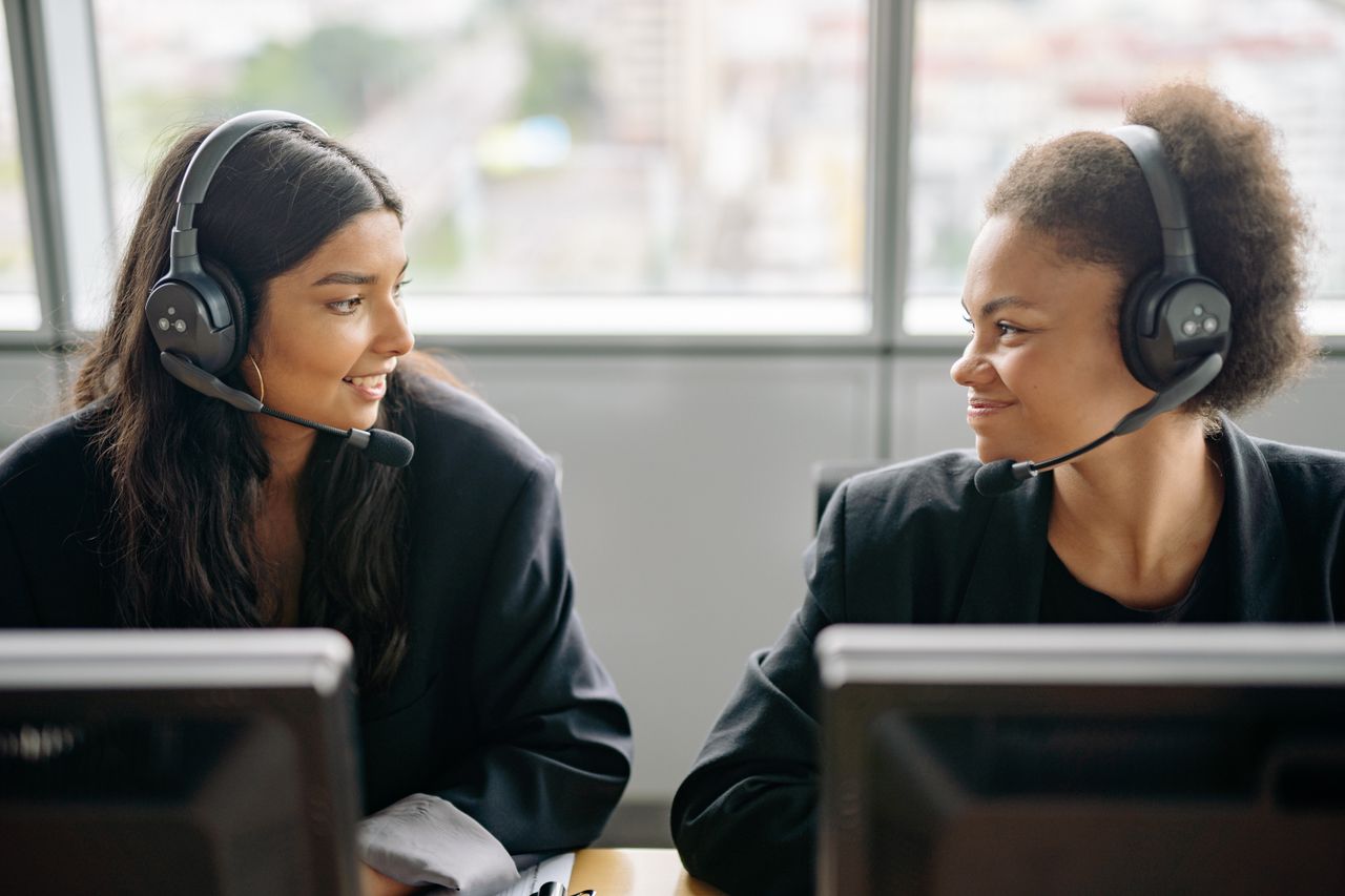 Two smiling female call center agents with headsets engaging in teamwork.